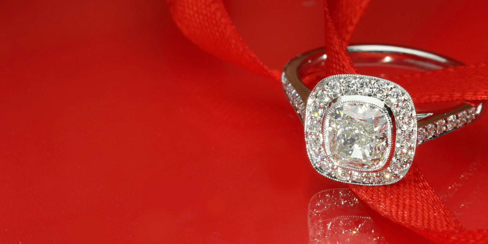 Cushion cut diamond halo engagement ring on a red ribbon background