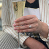 Celebrating a proposal with a glass of champagne and an oval diamond halo engagement ring